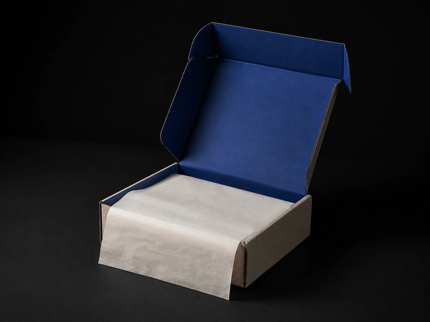A kraft corrugated e-commerce mailer, lid open, interior printed solid cobalt, bone tissue paper spilling over one edge