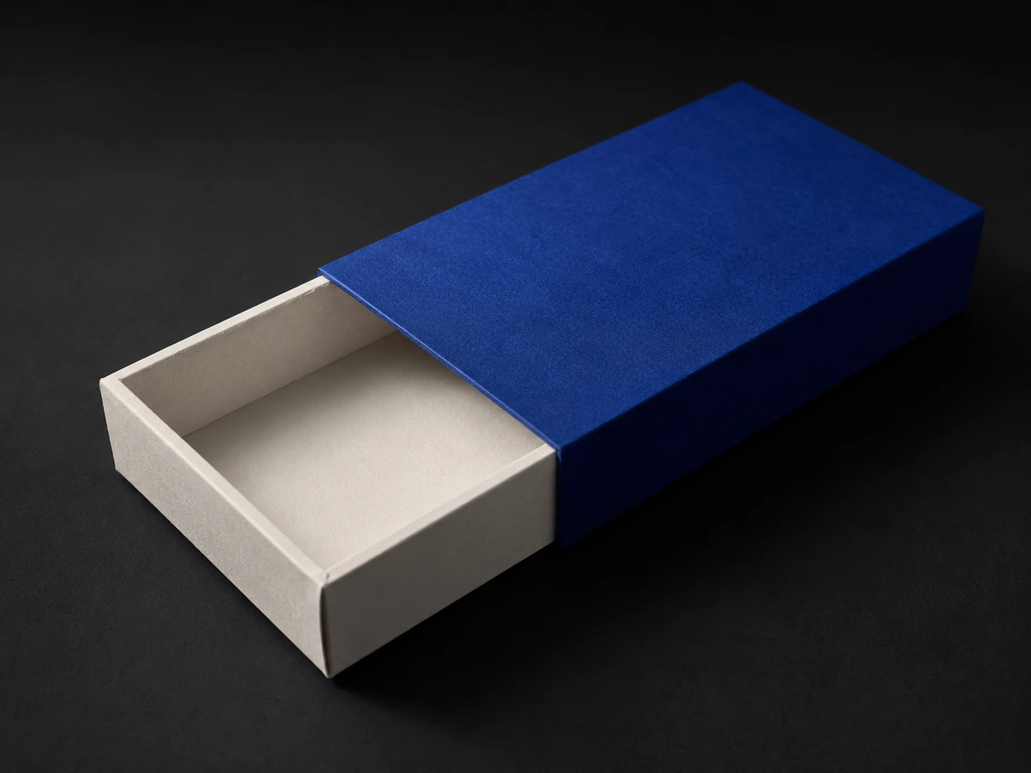 A solid cobalt printed sleeve half slid off a bone inner tray, the overlap seam and board thickness visible